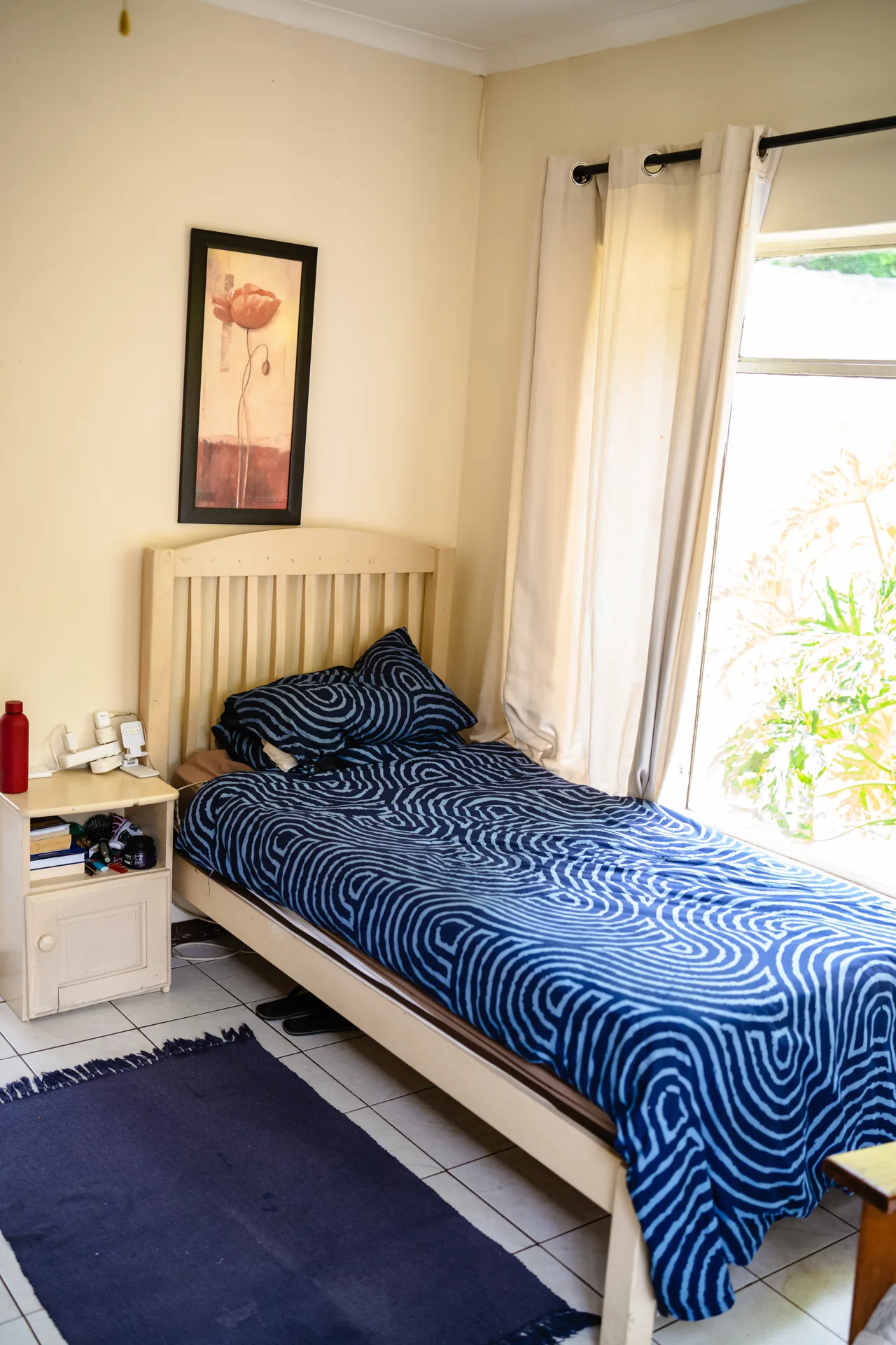 A light-filled bedroom with blue bedding and a window overlooking the garden