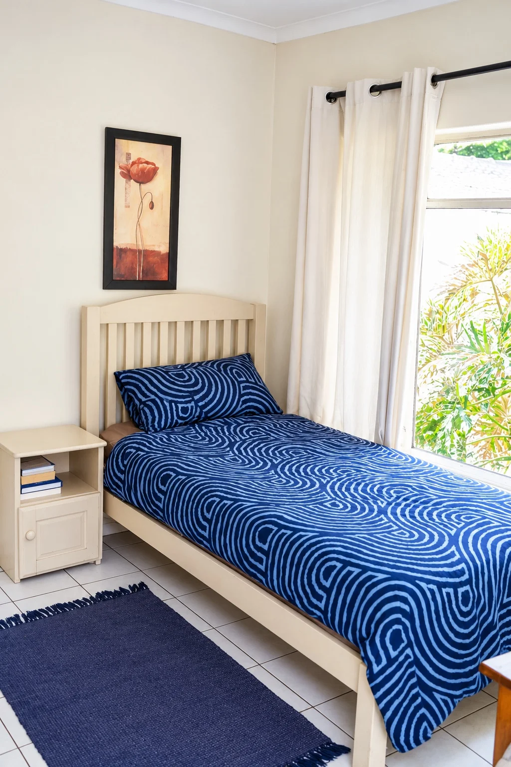 A light-filled bedroom with blue bedding and a window overlooking the garden
